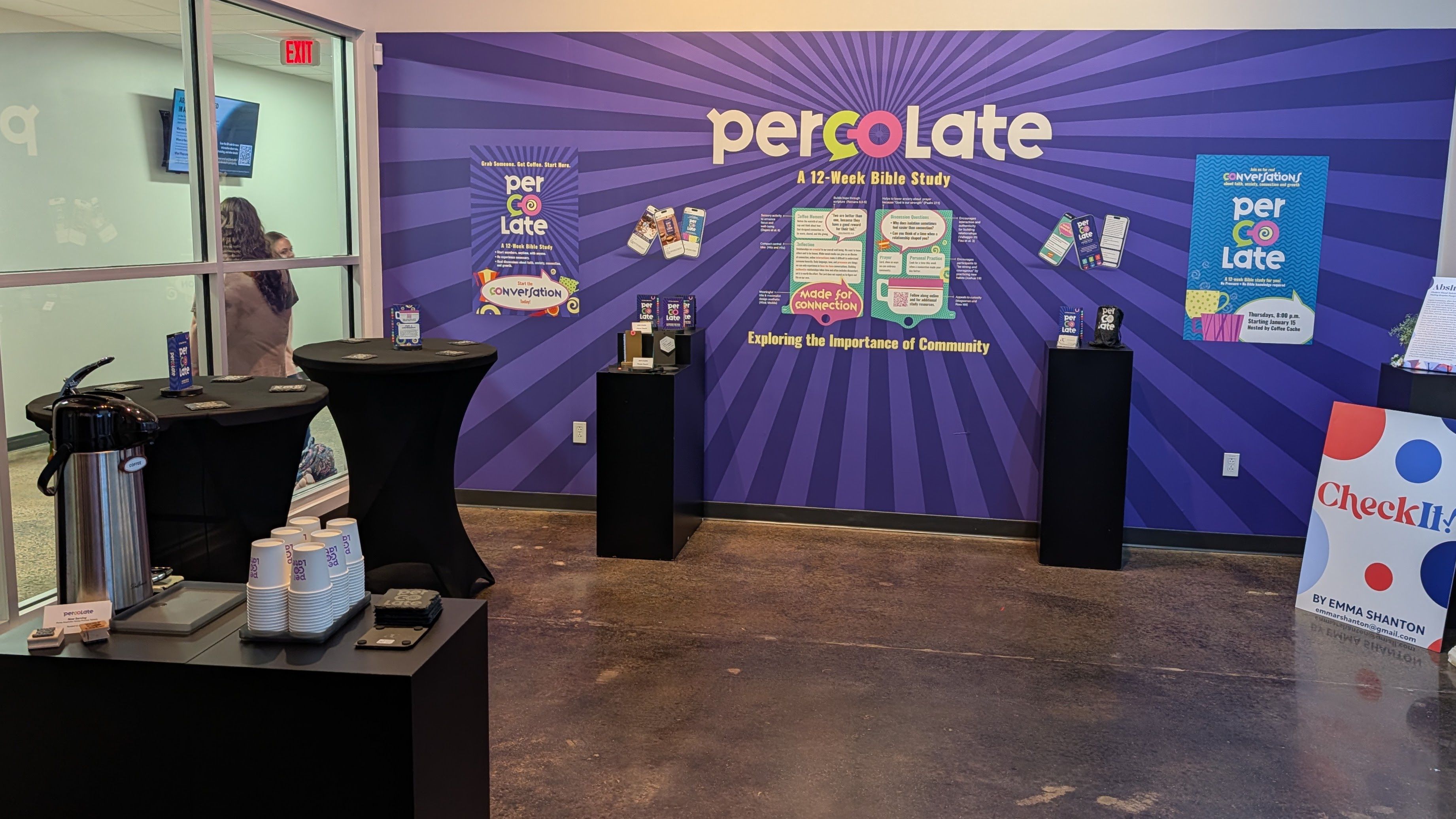 Percolate MFA thesis gallery exhibition at Liberty University — large purple wall mural with Percolate branding, pedestal displays showing the Bible study stand, and a coffee station for visitors